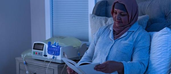 Malay dialysis patient reading beside an APD cycler machine